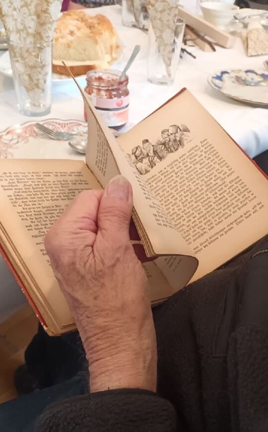 Hand einer Seniorin, die in einem Buch blättert.