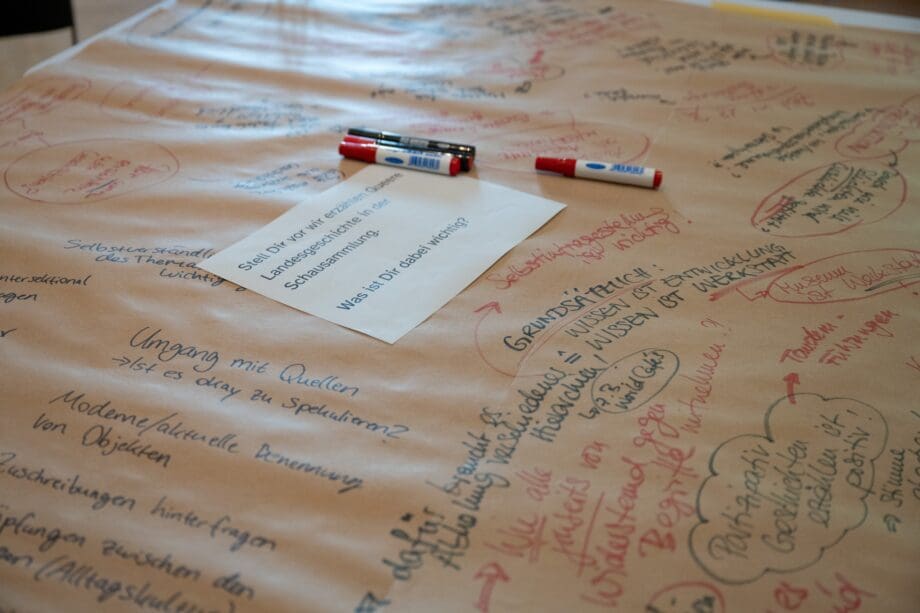 Ausschnitt aus einem beschriebenen Poster aus einem Workshop mir Kommentarenin verschienden Farben. Auf dem Poster liegen verschiedenen Stifte.